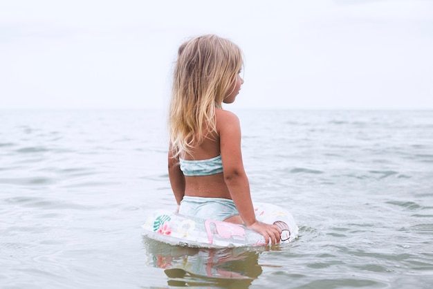 Blondes Mädchen des Kindes mit einem aufblasbaren Ring badet im Meer