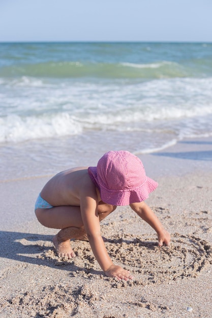 Blondes Mädchen des Kindes zieht auf den Sand am Strand