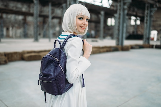 Blondes Mädchen im Anime-Stil mit Rucksack. Cosplay, japanische Kultur, Puppe im Kleid auf verlassener Fabrik