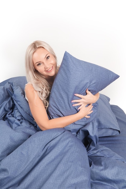 Blondes Mädchen im Bett mit weißen Kissen und einer Decke in einem hellen Schlafzimmer, Heimtextilien