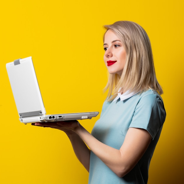 Blondes Mädchen im blauen Kleid mit Laptop-Computer auf gelbem Raum