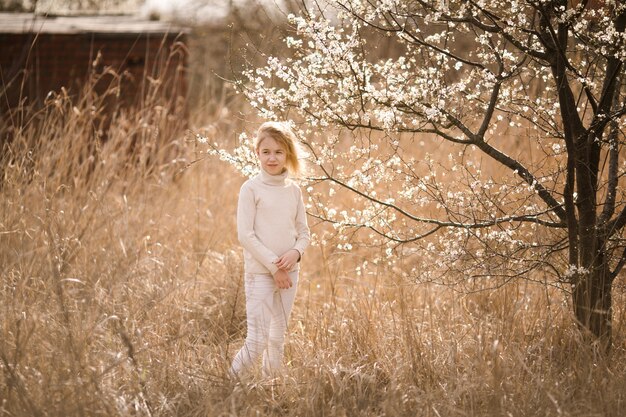 Blondes Mädchen im Blütengarten. Frühlingshintergrund mit weißer Blume