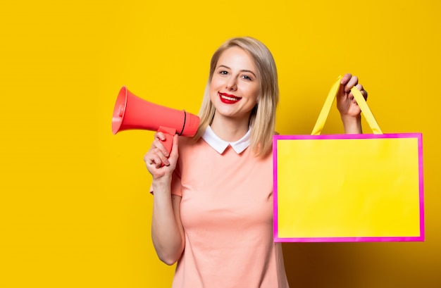 Blondes Mädchen im rosa Kleid mit Einkaufstasche und Megaphon