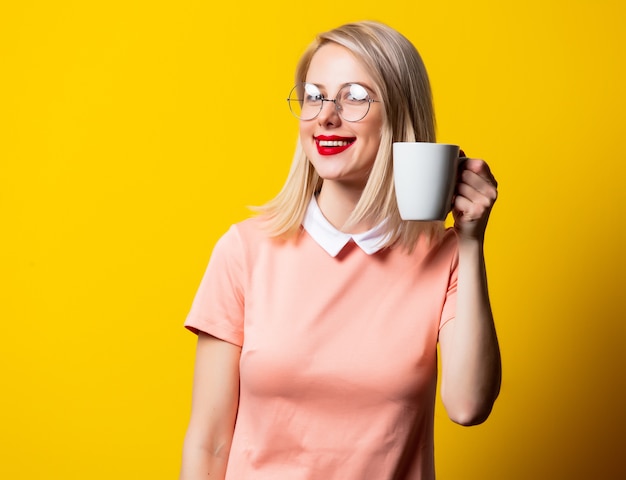 Blondes Mädchen im rosa Kleid mit Tasse Kaffee auf gelbem Hintergrund