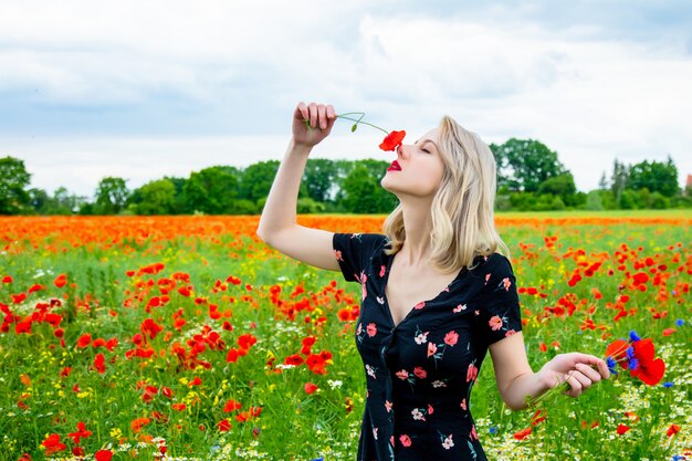 Blondes Mädchen im schönen Kleid im Mohnfeld in der Sommerzeit