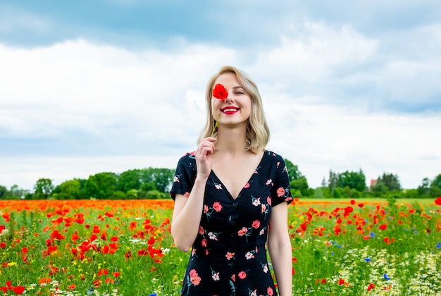 Blondes Mädchen im schönen Kleid im Mohnfeld in der Sommerzeit