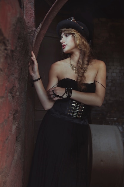 Blondes Mädchen im schwarzen Kleid an einer alten verlassenen Fabrik. Steampunk