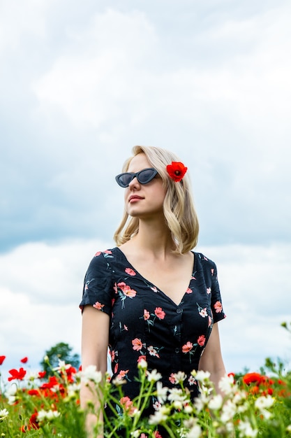 Blondes Mädchen in der Sonnenbrille im Mohnfeld in der Sommerzeit