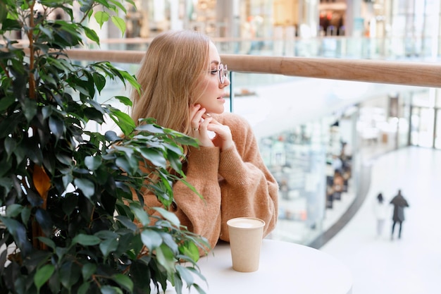 Blondes Mädchen in einem Einkaufszentrum, das Kaffee aus einer Craft-Tasse trinkt