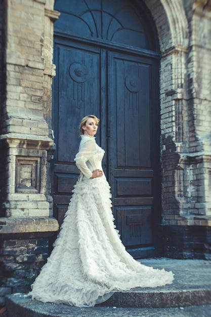 Blondes Mädchen in einem Retro-Kleid auf dem Hintergrund der alten dunklen Tür des Gebäudes