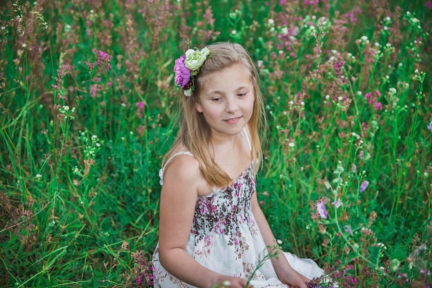 Blondes Mädchen in einem Sommerkleid sitzt in Blumen