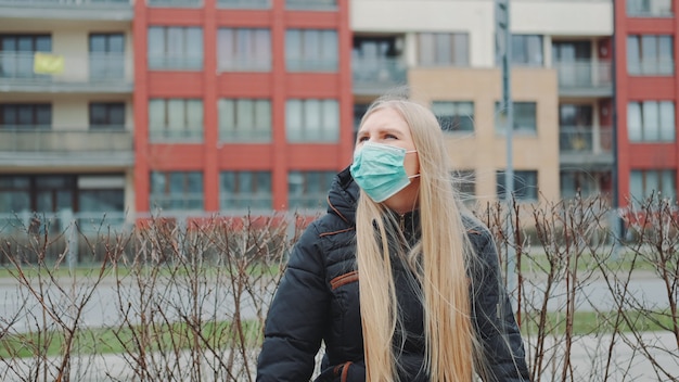 Foto blondes mädchen in einer medizinischen maske, die auf der bank sitzt.