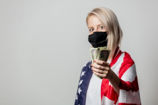 Blondes Mädchen in Gesichtsmaske mit USA-Flagge und Geld