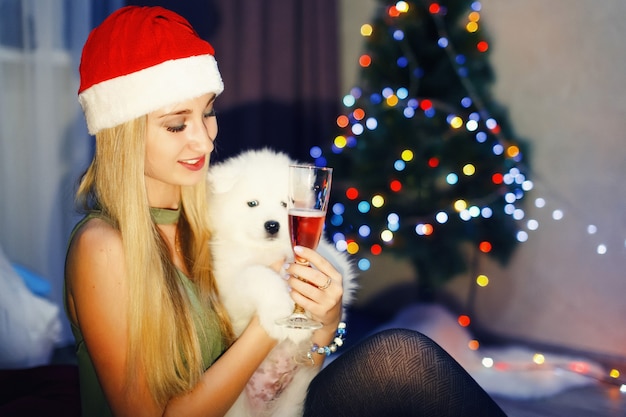 Blondes Mädchen in roter Weihnachtsmütze mit Samojede-Husky-Hund in Weihnachtsdekorationen