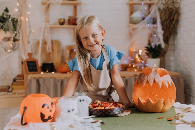 Blondes Mädchen in Schürze in der Küche mit Kürbissen für Halloween dekoriert bereitet einen Focaccia-Kuchen zu