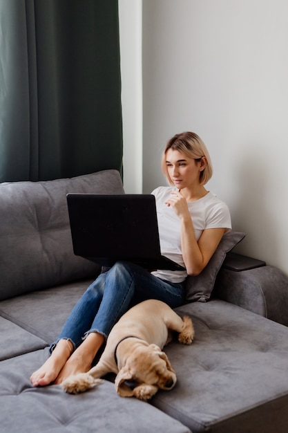 blondes Mädchen mit einem Hund, der auf der Couch mit einem Laptopplatz für Text sitzt