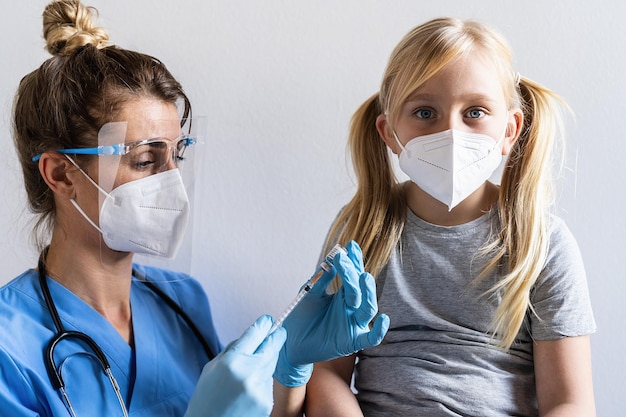 Blondes Mädchen mit Gesichtsmaske sieht erstaunt aus, als das Impfzentrum geimpft wird Spritze mit Impfstoff gegen gefährliche Infektionskrankheiten der Covid19-Coronavirus-Grippe