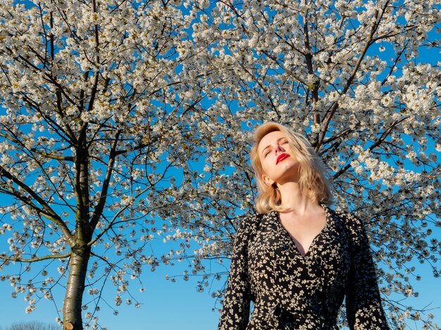 Blondes Mädchen nahe blühendem Baum an der Landschaft im Sonnenuntergang