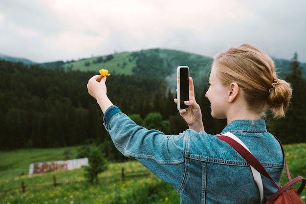 Blondes Mädchen schießt Blume am Telefon in den Bergen der Karpaten