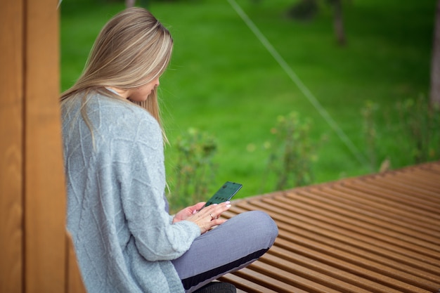 Blondes Mädchen sitzt auf einer Bank und untersucht ein Smartphone