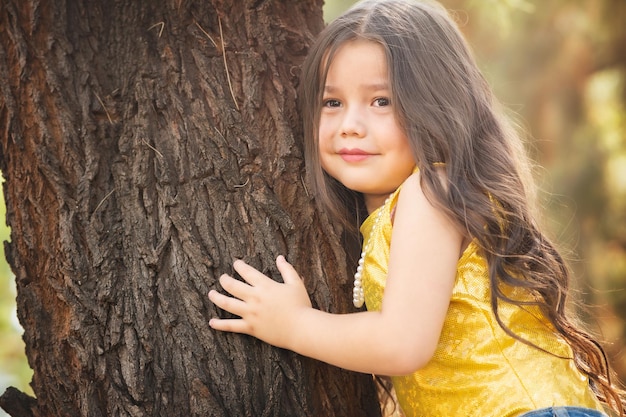 Blondes Mädchen umarmt einen Baum mit glücklichem Gesichtsausdruck. Kindertag-Thema Internationaler Baumtag