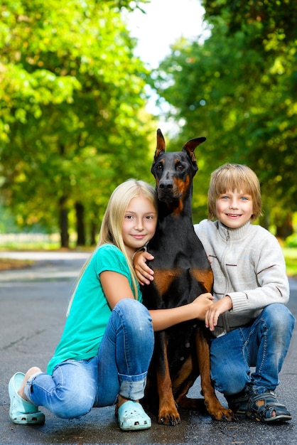 Blondes Mädchen umarmt ihren geliebten Hund im Sommerpark mit Bruder