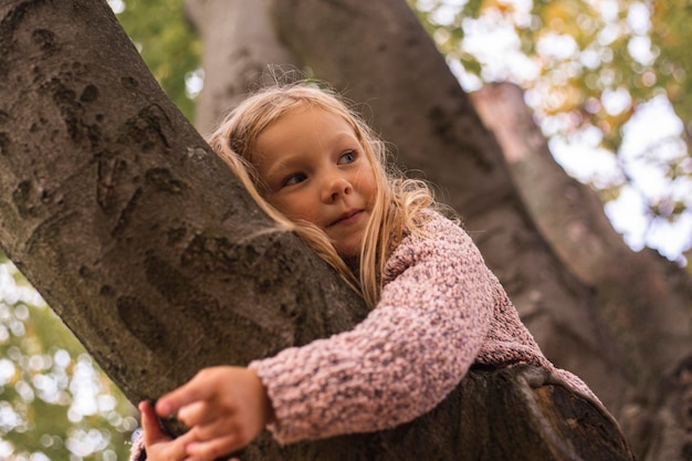 Blondes Mädchen umarmt mit zwei Händen einen Baum im Park