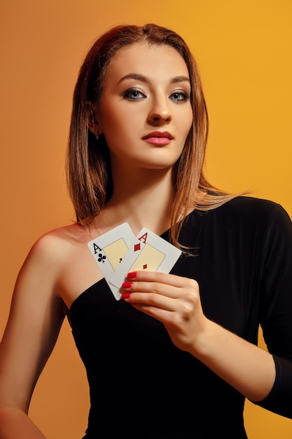 Blondes Model mit hellem Make-up im schwarzen Kleid zeigt zwei Asse posieren