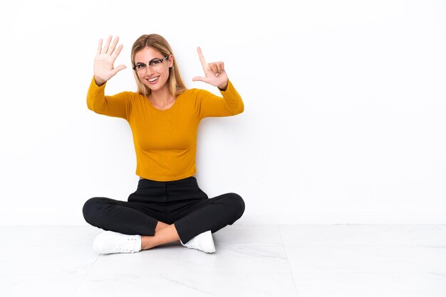 Blondes uruguayisches Mädchen, das auf dem Boden sitzt und mit den Fingern sieben zählt