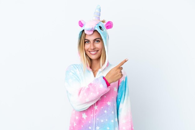 Blondes uruguayisches Mädchen, das einen Einhornpyjama trägt, isoliert auf weißem Hintergrund, der zur Seite zeigt, um ein Produkt zu präsentieren