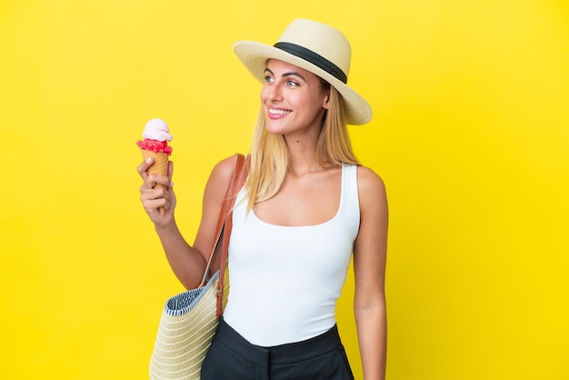 Blondes uruguayisches Mädchen hält im Sommer Eis isoliert auf gelbem Hintergrund, schaut zur Seite und lächelt