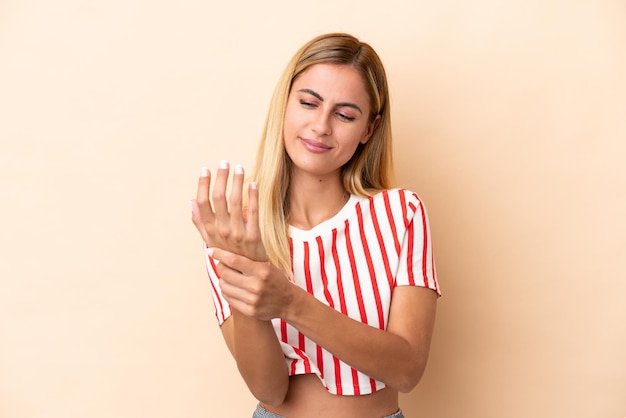 Blondes uruguayisches Mädchen isoliert auf beigefarbenem Hintergrund, das unter Schmerzen in den Händen leidet