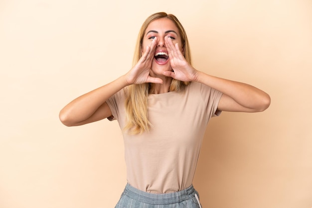 Blondes uruguayisches Mädchen isoliert auf beigem Hintergrund, das etwas schreit und ankündigt