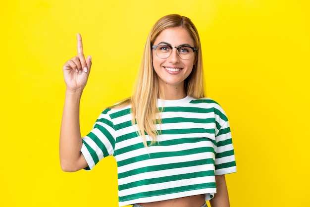 Blondes uruguayisches Mädchen isoliert auf gelbem Hintergrund, das auf eine großartige Idee zeigt