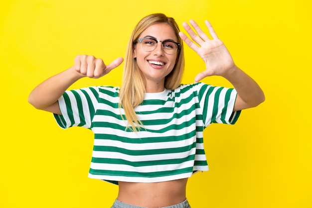 Blondes uruguayisches Mädchen isoliert auf gelbem Hintergrund, das sechs mit den Fingern zählt