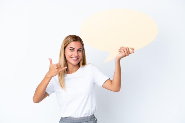 Blondes uruguayisches Mädchen isoliert auf weißem Hintergrund, das eine leere Sprechblase hält und Telefongeste macht