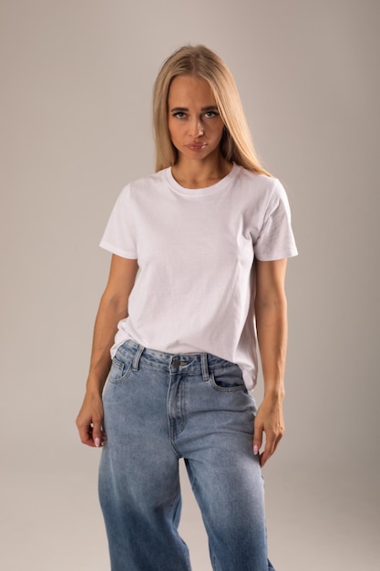 Blondin in weißem T-Shirt und Jeans posiert auf weißem Hintergrund