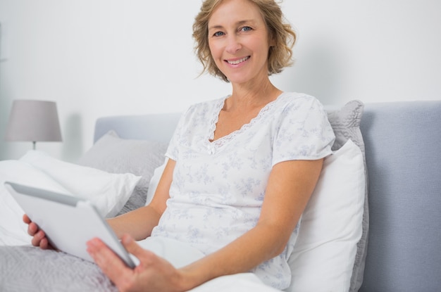 Blondine, die im Bett unter Verwendung des Tabletten-PC sitzen