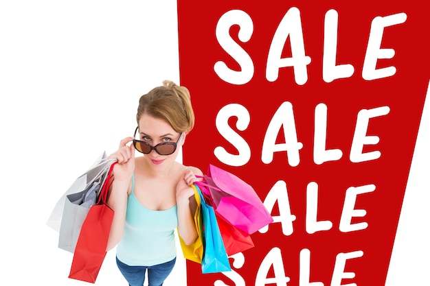 Blondine, die über ihre Sonnenbrille schaut, während sie Taschen gegen Verkaufsanzeige hält