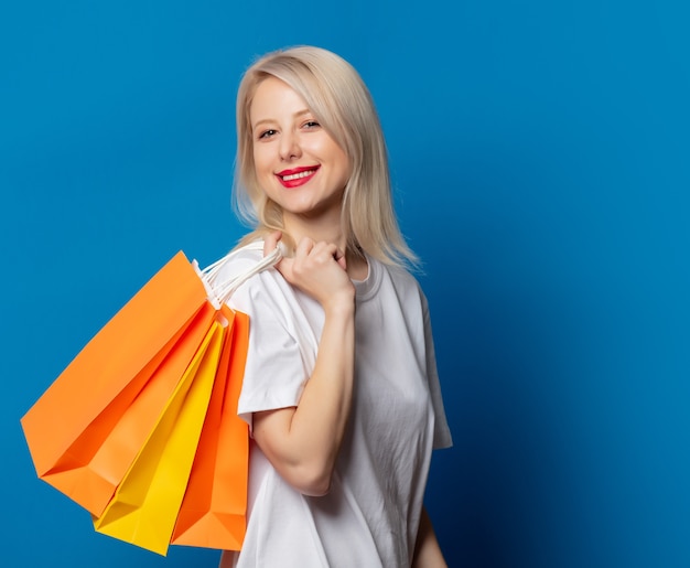 Blondine im weißen T-Shirt mit Einkaufstaschen auf blauem Raum