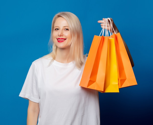 Blondine im weißen T-Shirt mit Einkaufstaschen auf blauem Raum