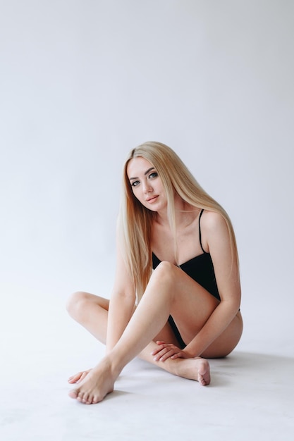 Blondine in der schwarzen Wäsche, die barfuß auf weißem Hintergrund mit Betonung auf ihren vertikalen Beinen aufwirft