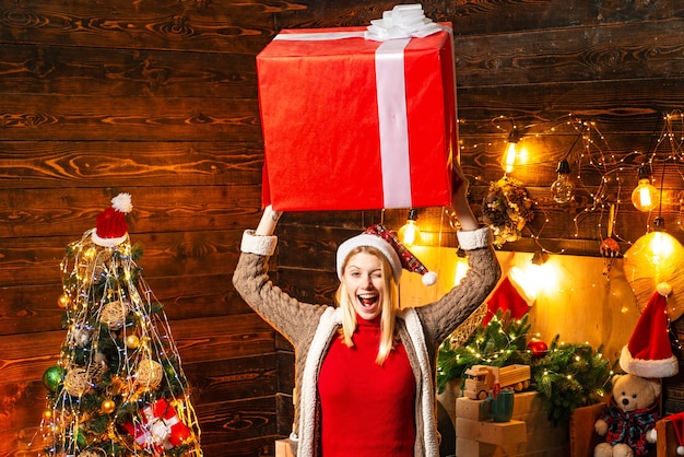 Blondine in der Weihnachtsmütze und in den Geschenken, die Weihnachtsferien feiern, die große Kiste haben