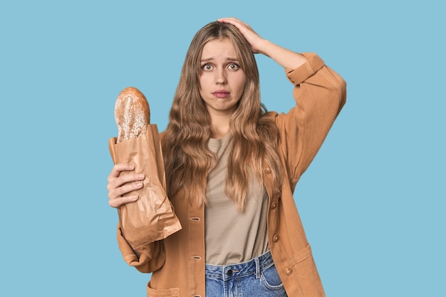 Blondine mit einem Brot im Studio ist schockiert, dass sie sich an ein wichtiges Treffen erinnert hat.