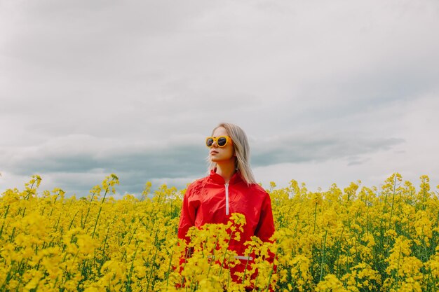 Blondine mit Sonnenbrille und rotem Trainingsanzug im Rapsfeld