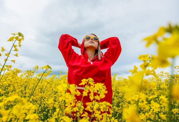 Blondine mit Sonnenbrille und rotem Trainingsanzug im Rapsfeld