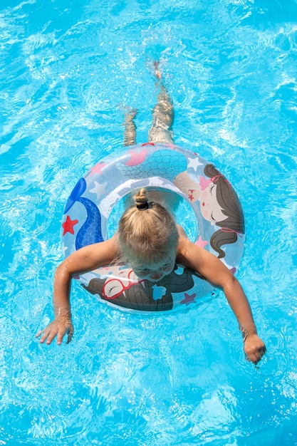 Blondine schwimmt mit einem aufblasbaren Ring im Pool, liegt oben und liegt flach.