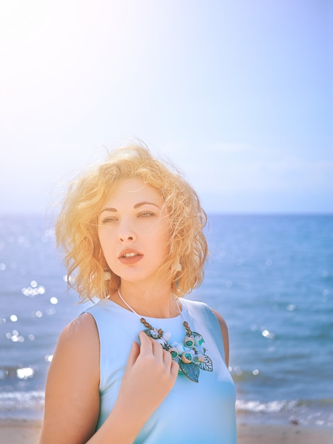 Blondy Frau der Sinnlichkeit im cyan-blauen Kleid am Strand