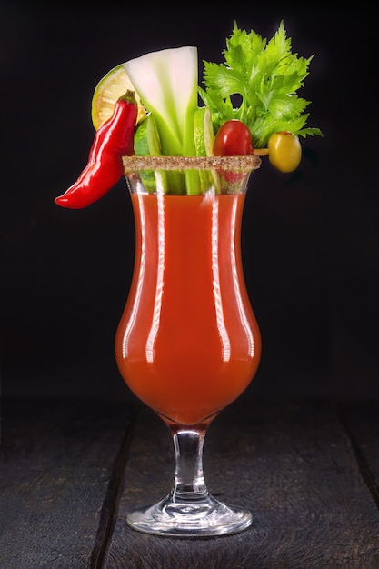 Bloody Mary, una bebida roja a base de vodka, jugo de tomate, jugo de limón, apio, guisantes, salsa y pimienta, sobre una superficie negra