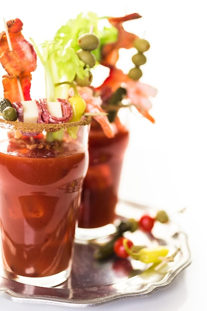 Bloody Mary Cocktail garniert mit Selleriestangen, Oliven und Speckstreifen.